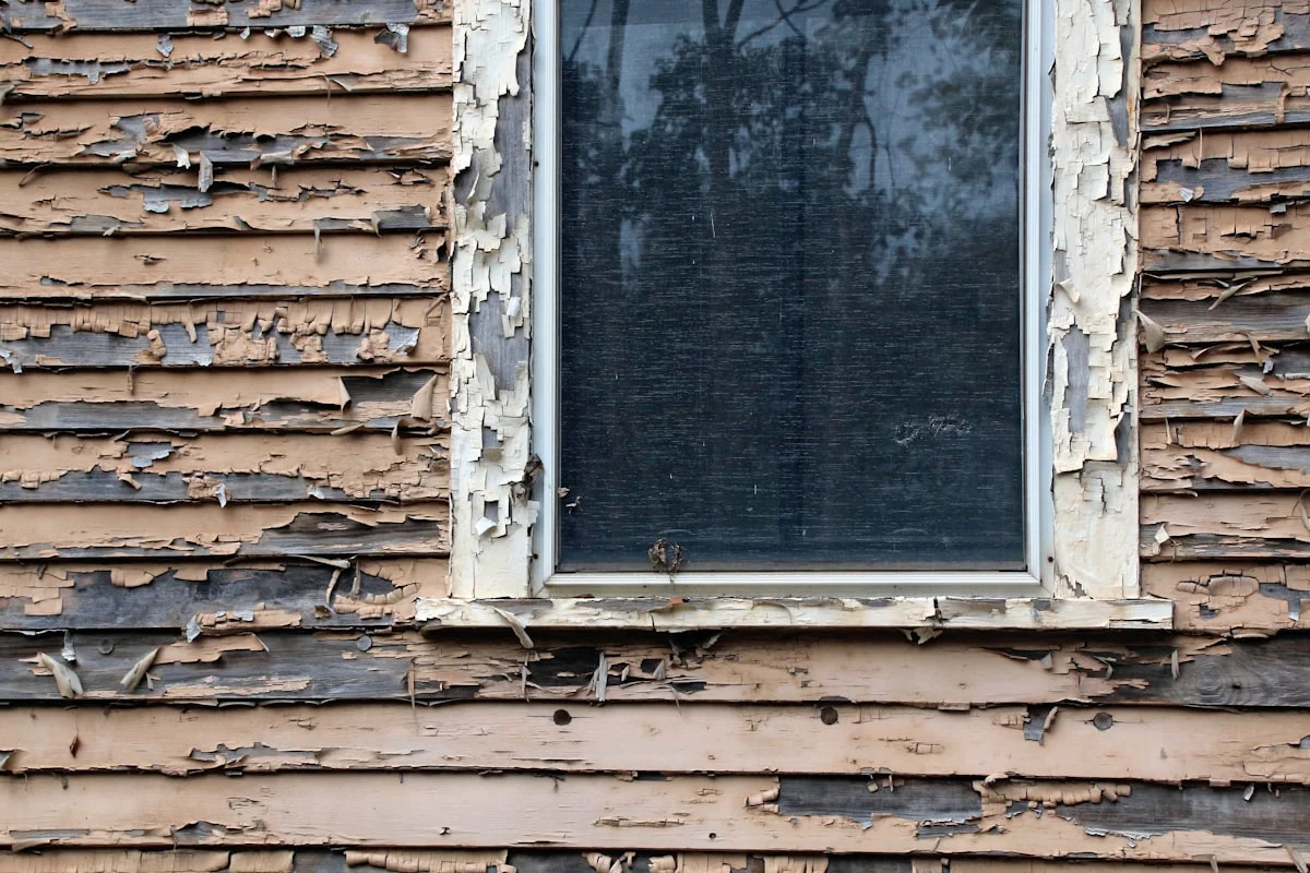 Peeling exterior paint and a weathered window on a New Jersey home